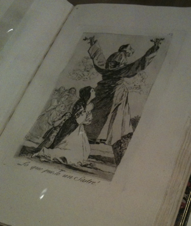 An antique sketchbook open to a page with a pen drawing by Francisco Goya, showing a hooded figure looming over a penitent girl.